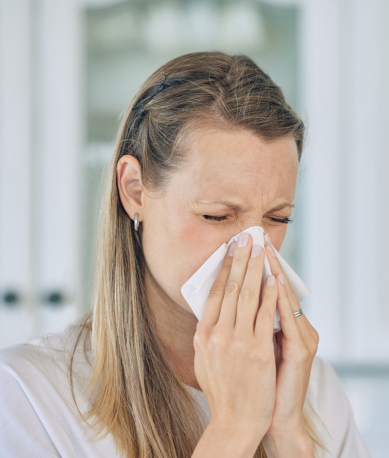 woman suffering from allergies with her eyes closed tightly andblowing her nose