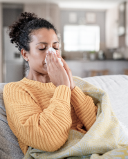 Woman on a couch suffering from allergies and blowing her nose