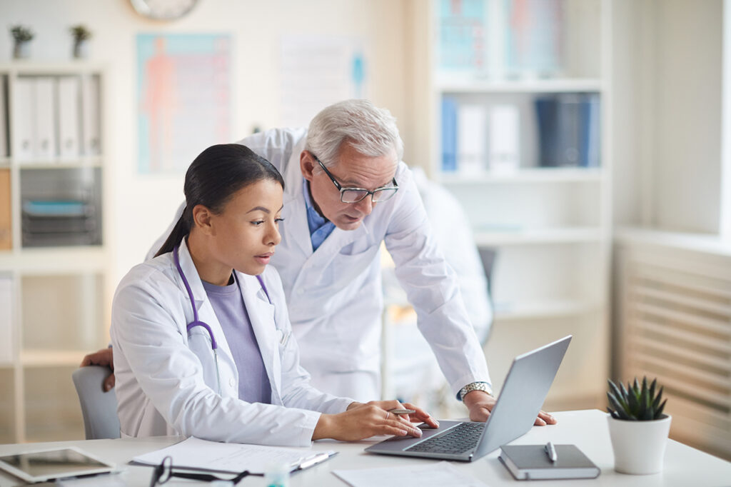 Two doctors, one male and one female, collaborating and reviewing patient data on a laptop in a medical office.