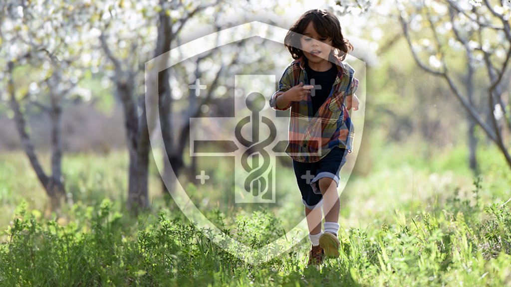 A young child running through a lush green orchard with the symbol of medical safety superimposed on the image, combining a shield and a medical cross.