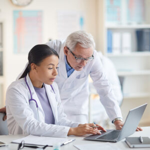 Two doctors in lab coats collaborating while working on a laptop in a medical office